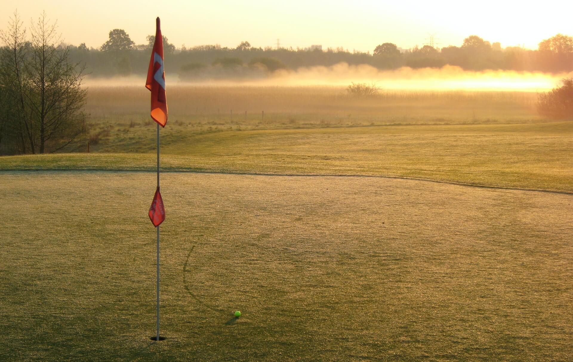 Ball near a golf hole on a golf course during sun set