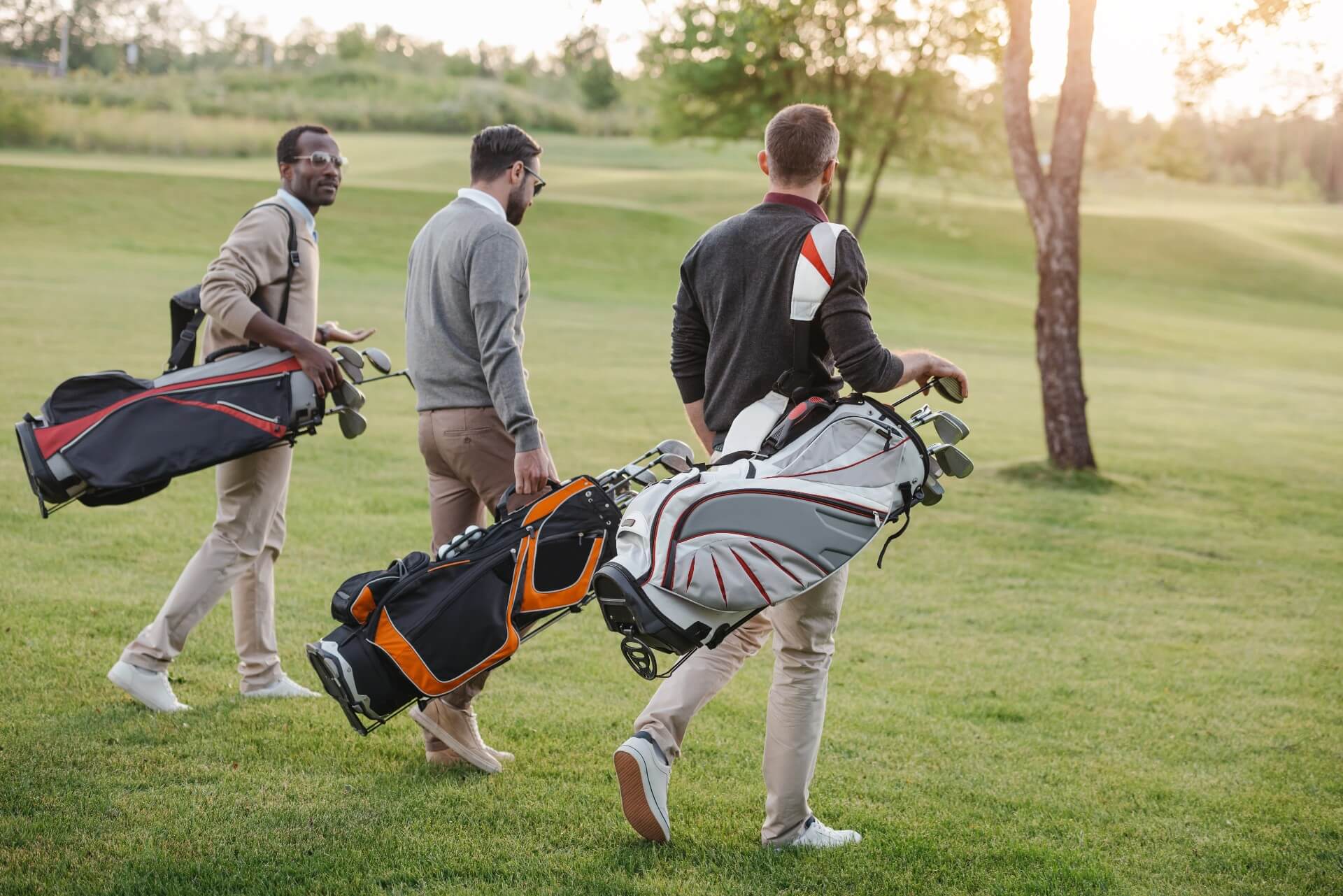 Three golf players walking with their golf tour bags on a golf course