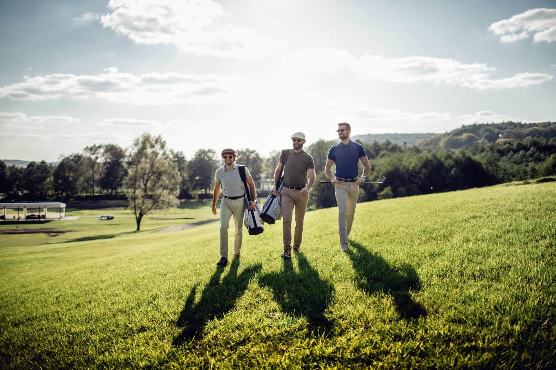 Three golf players walking with their golf tour bags on a golf course