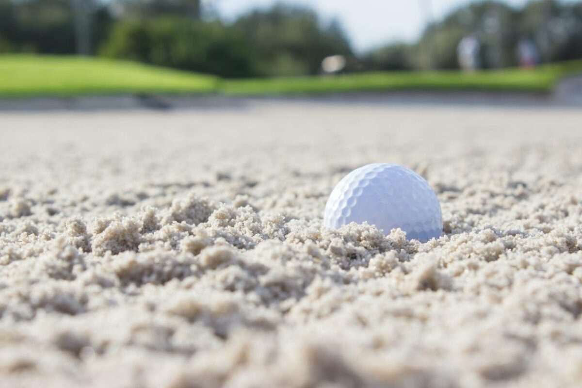 Close up picture of a golf ball on a sand pit