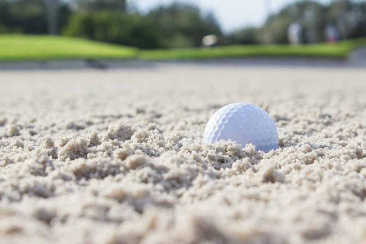 Close up picture of a golf ball on a sand pit