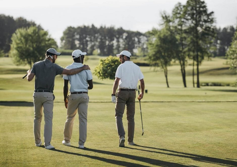 Three golf players walking with their golf clubs on a golf course Three golf players walking with their golf clubs on a golf course