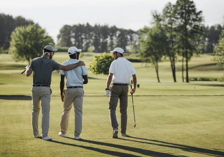 Three golf players walking with their golf clubs on a golf course